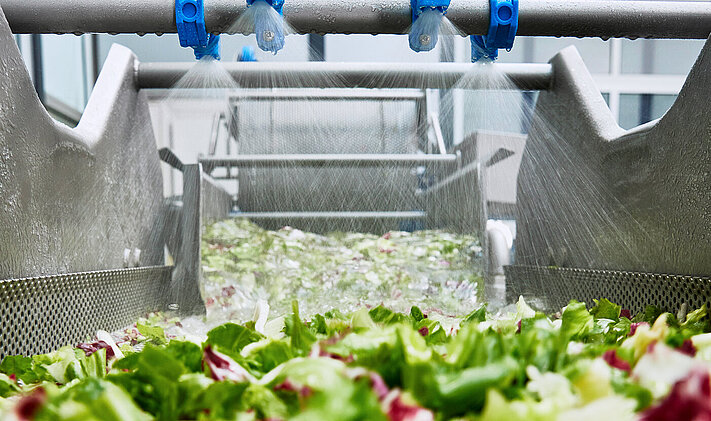 Fresh water spray of the HEWA washing machines from KRONEN rinses and cleans the product during discharge out of the machine